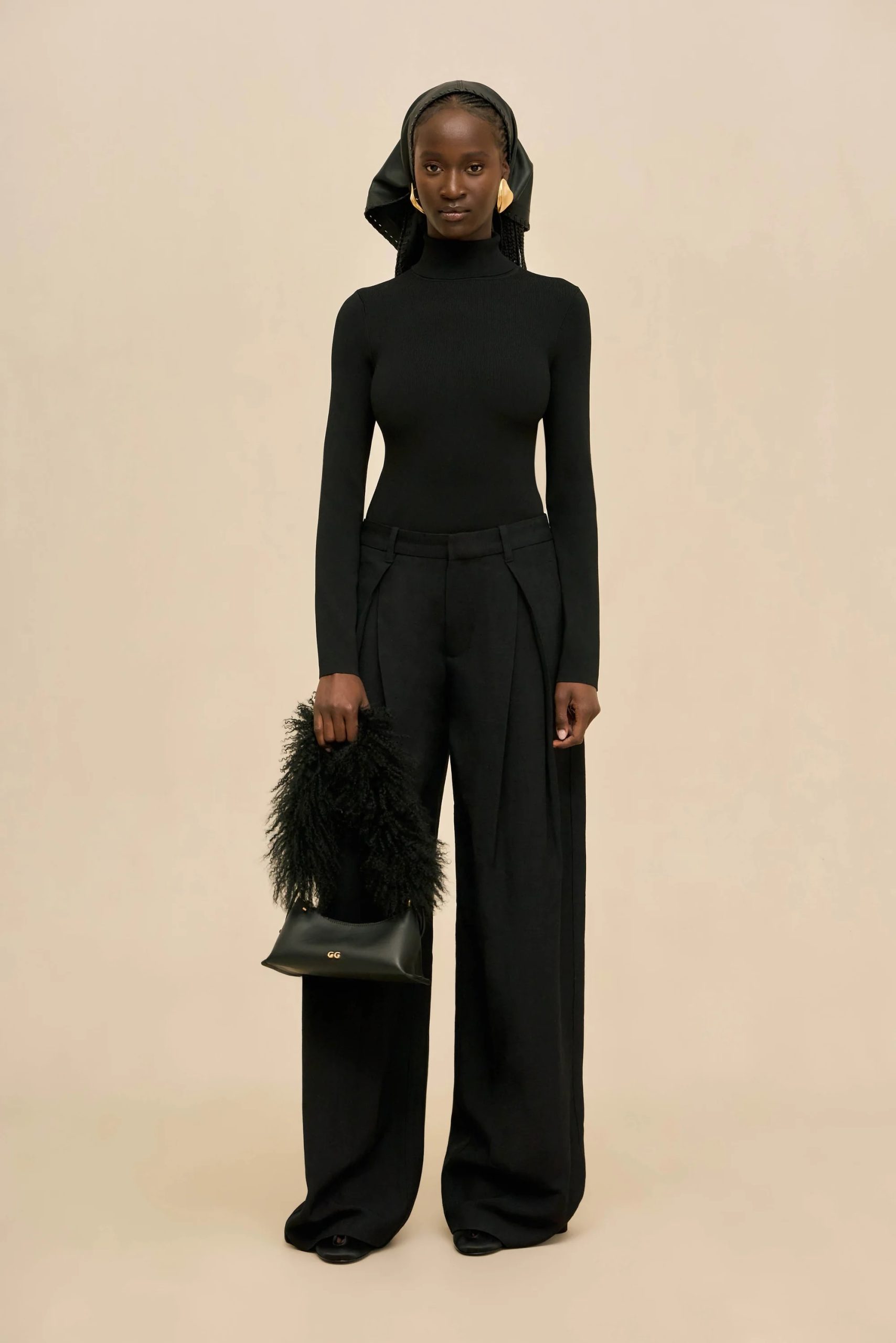Image 407 - New Trend Model wearing a fitted black turtleneck and wide-leg trousers with a black headscarf, standing against a beige backdrop.