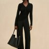 Image 409 - New Trend Woman in an all-black outfit (ribbed long-sleeve top and wide-leg pants) wearing oversized sunglasses and gold earrings, carrying a black handbag with a chain strap against a beige backdrop.