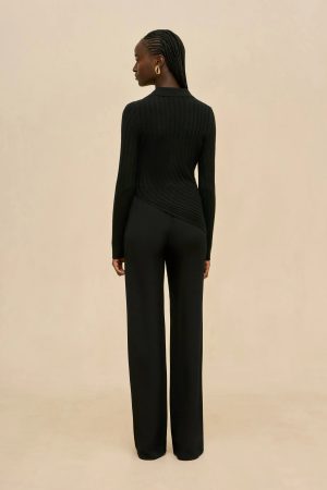 Back view of a person in a black ribbed sweater and wide-leg black pants against a beige backdrop.