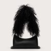 Back view of a person with long curly black hair draped over a black leather handbag with a small GG logo, against a pale background.