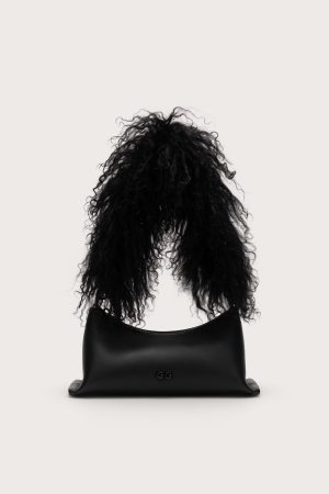 Back view of a person with long curly black hair draped over a black leather handbag with a small GG logo, against a pale background.