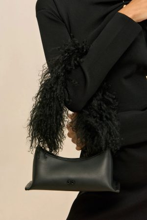 Close-up of a person in a black sweater holding a black leather handbag with a 'GG' logo against a light background.