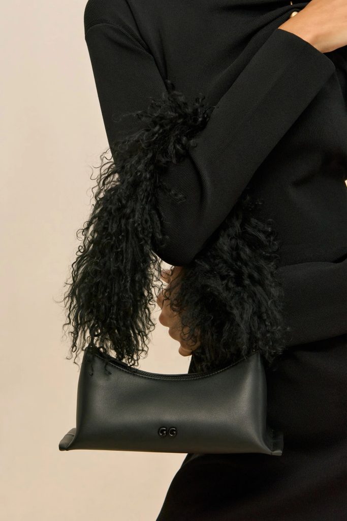 Close-up of a person in a black sweater holding a black leather handbag with a 'GG' logo against a light background.