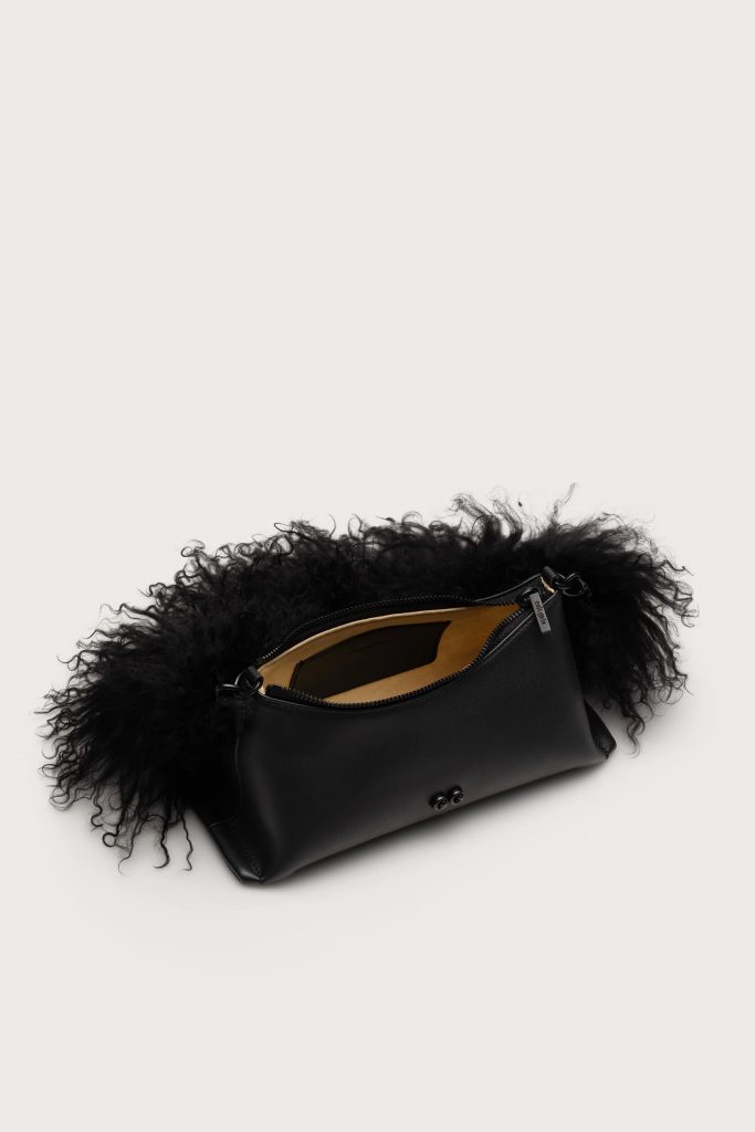 Black leather handbag with a fluffy black fur trim around the opening on a pale background, showing a tan interior.