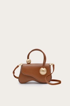 Brown leather handbag with two large gold-toned spheres attached to handles, on a light beige background