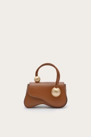 Brown leather handbag with curved top, double handles, and large gold sphere accents on the handles against a light background.
