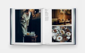 Open book spread: left page shows a server pouring drinks from a tray, right page features a cozy living room and a round dining table set with plates and dishes.