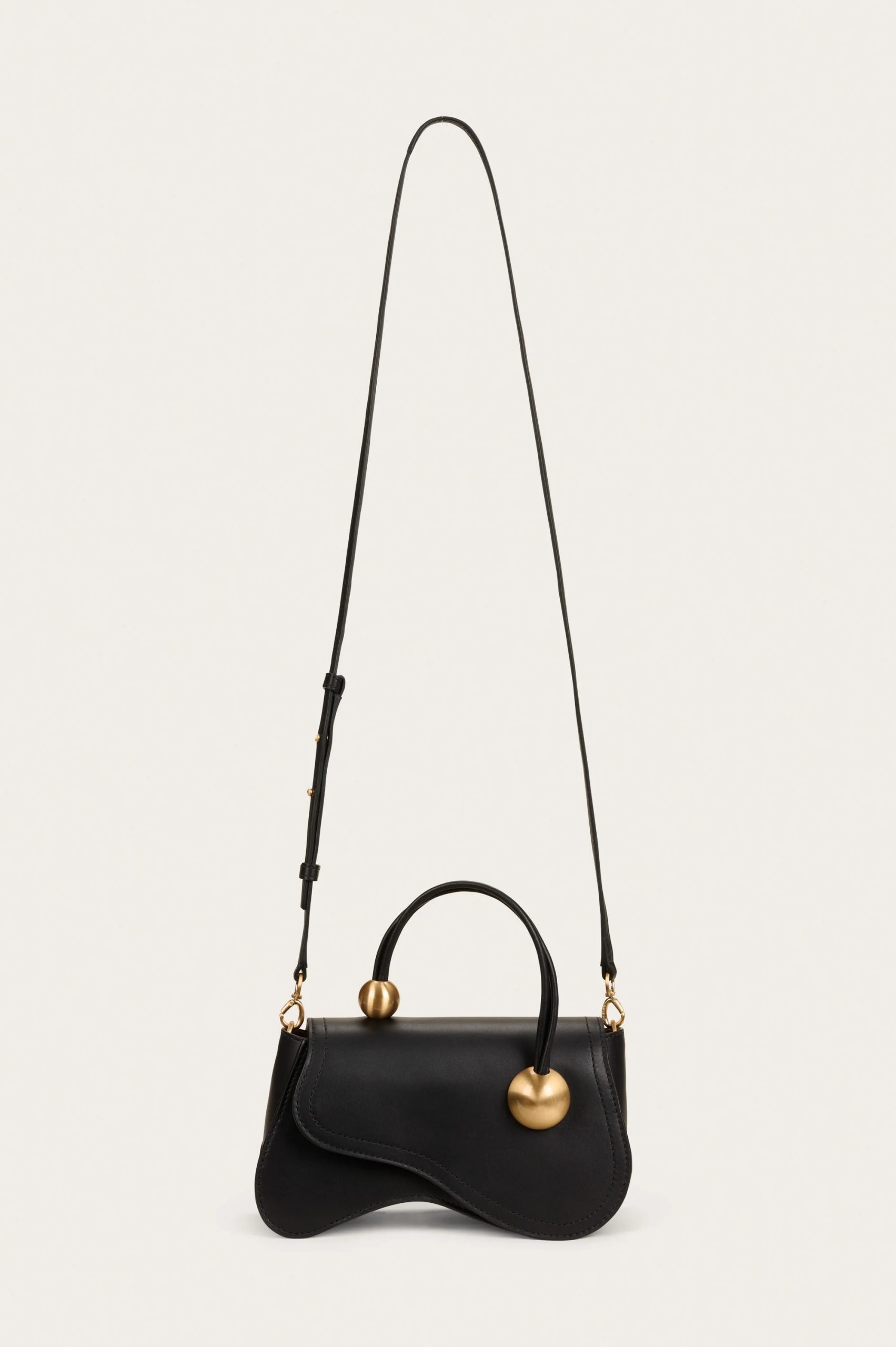 Image 443 - New Trend Black handbag with a curved flap and gold spherical hardware hanging from thin straps against a white background