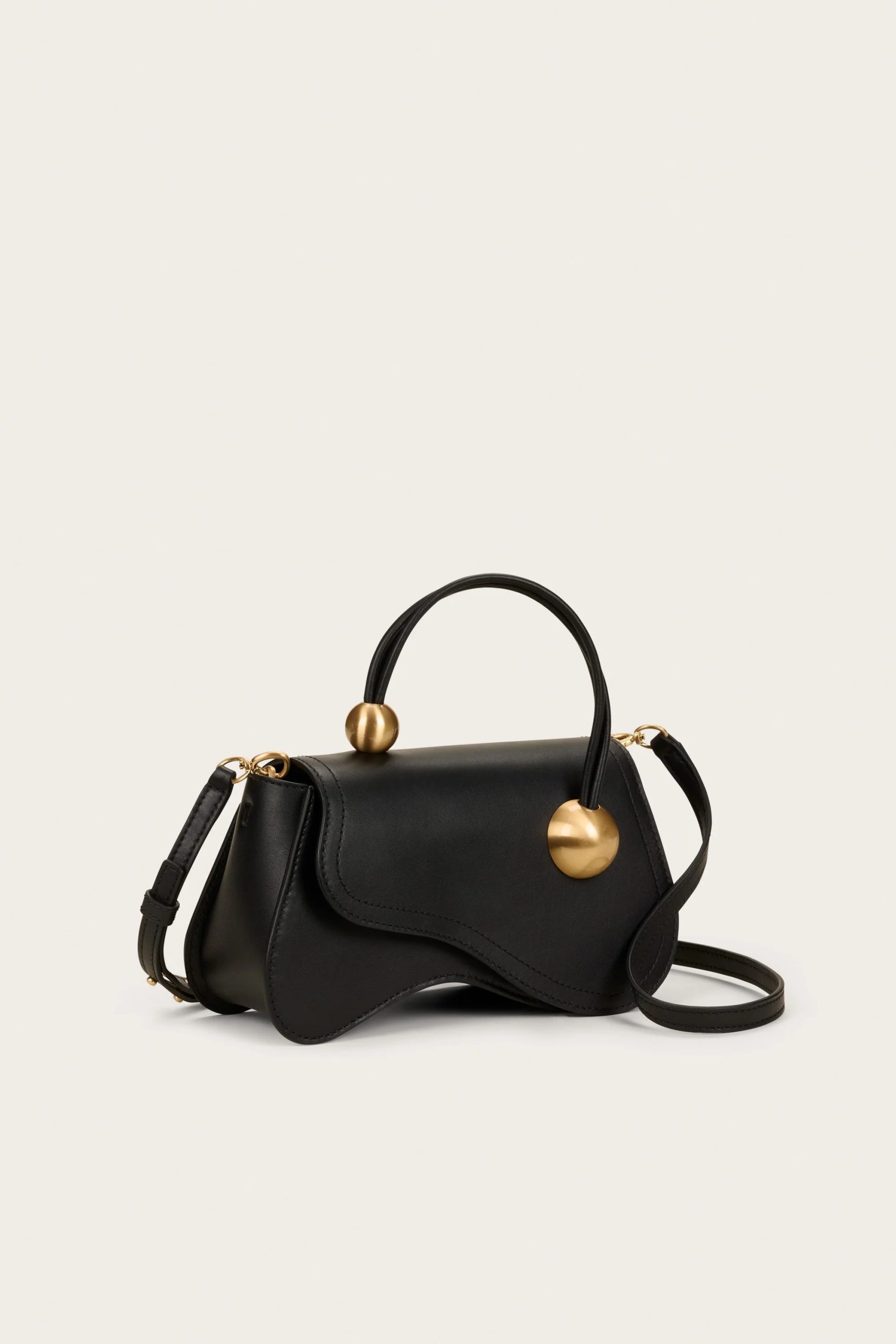 Image 444 - New Trend Black leather handbag with gold spherical hardware on the handles, placed against a pale background.