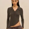 Woman standing against a beige background, wearing a dark ribbed knit top with a diagonal hem that exposes the midriff and striped drawstring pants, looking at the camera.