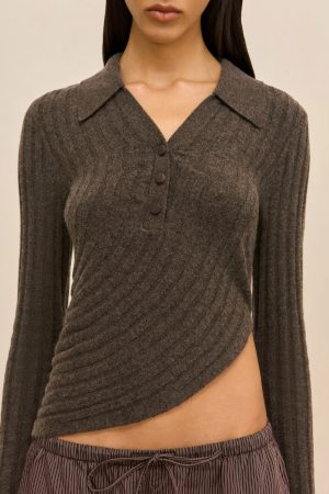 Close-up of a person wearing a dark gray ribbed knit top with a collar and three-button placket, paired with striped pants.