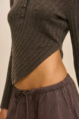 Close-up of a person wearing a dark gray ribbed cardigan with two buttons visible, and a high-waisted striped skirt at the hip.