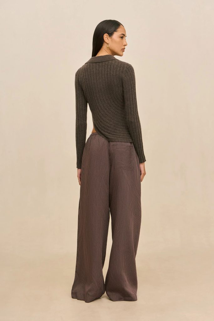 Person standing with back to camera, wearing a brown ribbed knit top and wide-leg striped pants against a neutral backdrop
