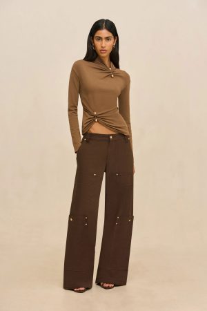 Woman in a brown twisted-front sweater and wide-leg brown cargo pants posing against a beige backdrop.