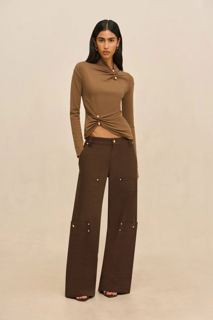 Woman in a brown twisted-front sweater and wide-leg brown cargo pants posing against a beige backdrop.