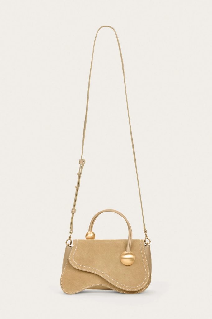 Beige handbag with top handle and long adjustable strap hanging against a light background.