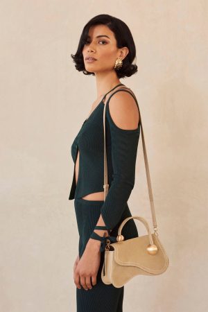 Side profile of a woman in a dark green ribbed outfit with an off-shoulder design, carrying a beige handbag.