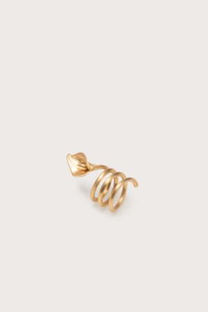 Gold-toned spiral ring with a leaf-shaped end, photographed on a pale beige background.