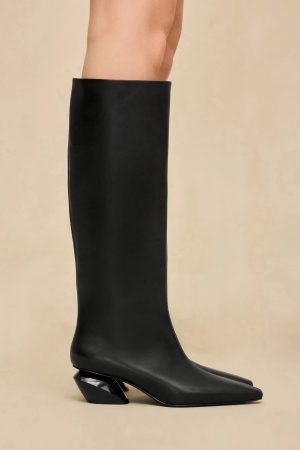 Black knee-high boot with a chunky angled heel, photographed from the side against a beige background
