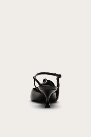 Front view of a glossy black high-heeled sandal with multiple straps and a tall stiletto heel, isolated on white/cream background.