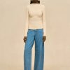 Model wearing a cream twisted-knit long-sleeve top with wide-leg jeans and snakeskin boots against a beige backdrop.