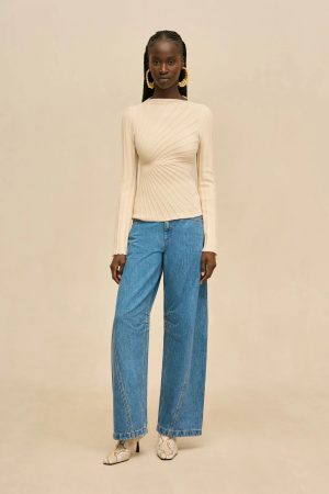 Model wearing a cream twisted-knit long-sleeve top with wide-leg jeans and snakeskin boots against a beige backdrop.