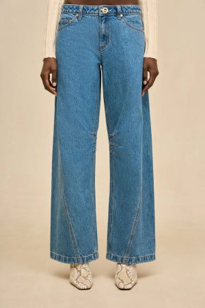Model wearing high-waisted blue wide-leg jeans with a beige knit top; snake-print boots visible at the bottom.