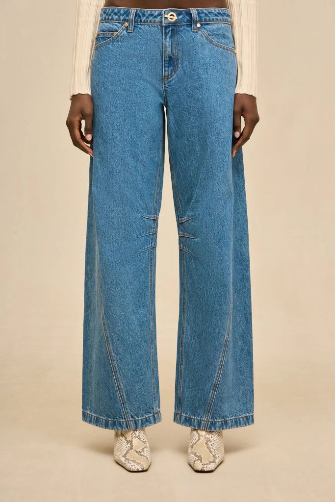 Model wearing high-waisted blue wide-leg jeans with a beige knit top; snake-print boots visible at the bottom.