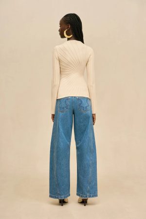 Back view of a woman wearing a beige ribbed long-sleeve top tucked into high-waisted wide-leg blue jeans, with braided hair and large circular gold earrings.