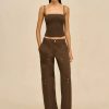 Model wearing a brown braided crop top with thin straps and brown cargo pants, standing against a beige background as a fashion shot.