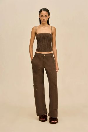 Model wearing a brown braided crop top with thin straps and brown cargo pants, standing against a beige background as a fashion shot.