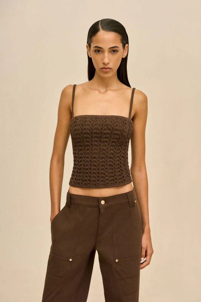 Model wearing a brown braided-knit crop top with thin straps and matching brown cargo pants against a neutral beige background.
