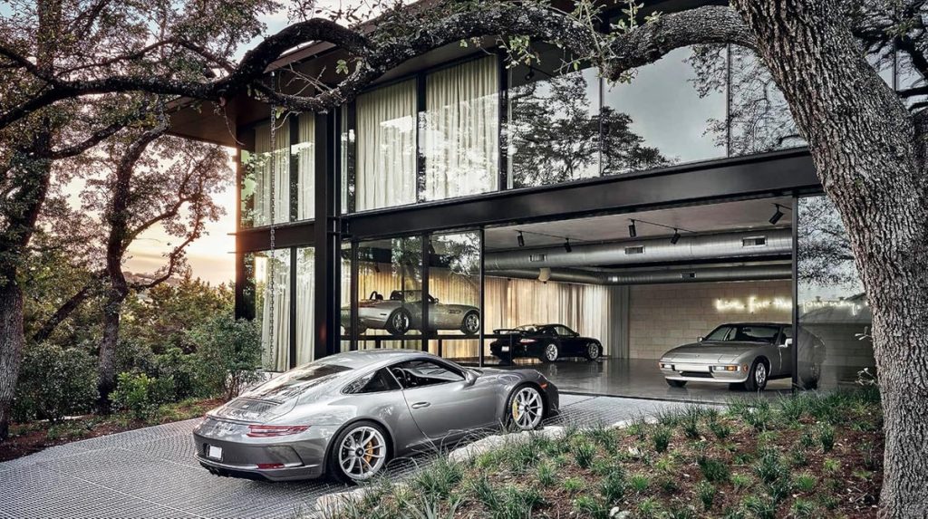 Modern glass-front garage displaying luxury cars; a silver sports car sits outside as others are visible inside the showroom.