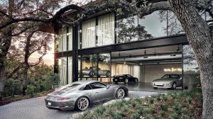 Modern glass-front garage displaying luxury cars; a silver sports car sits outside as others are visible inside the showroom.