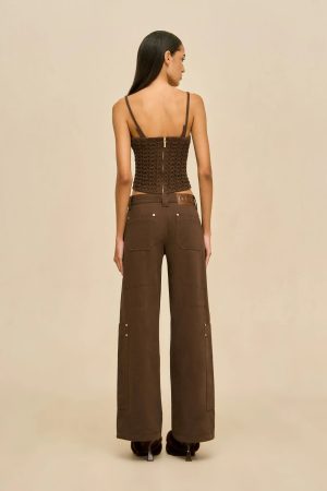 Back view of a woman wearing a brown lace-up corset top and wide brown pants against a beige backdrop.