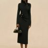 Image 501 - New Trend Full-length portrait of a woman in a black dress with gold buttons, holding a black handbag against a beige backdrop.