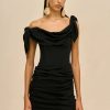 Model wearing a black off-shoulder draped dress with large gold teardrop earrings against a beige backdrop.