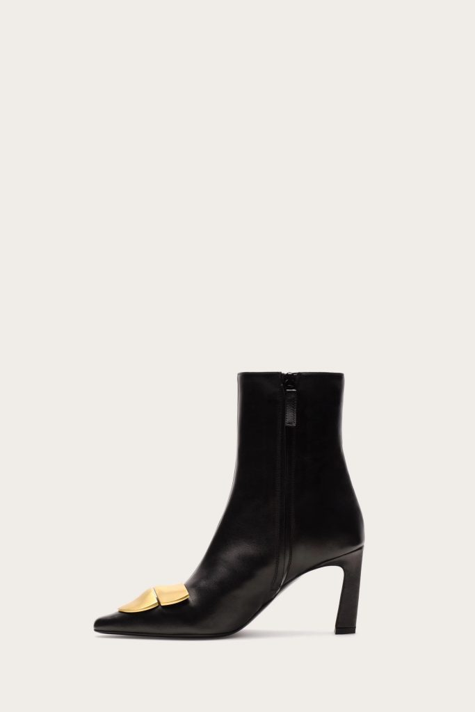 Black ankle boot with a gold-toned buckle on the vamp and a front zipper, high heel, against a light background.