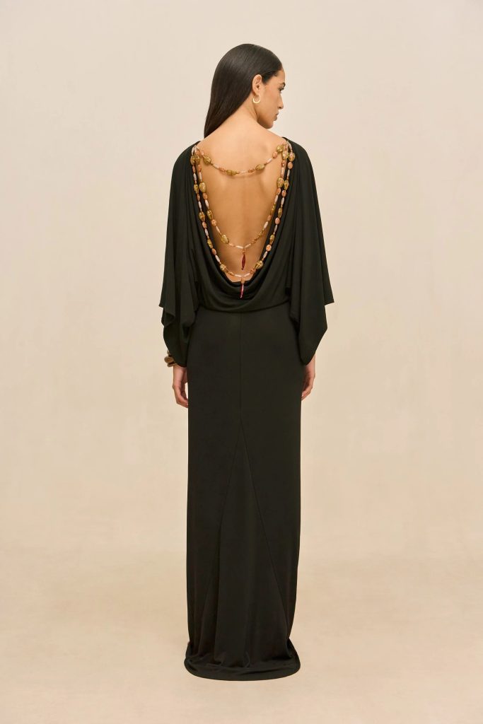 Back view of a woman in a long black gown with a deep open back and layered beaded necklace draping down her back.