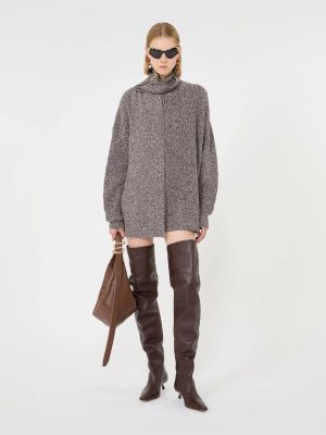 Model wearing an oversized gray knit turtleneck sweater dress with knee-high brown leather boots and a brown handbag, accessorized with sunglasses.