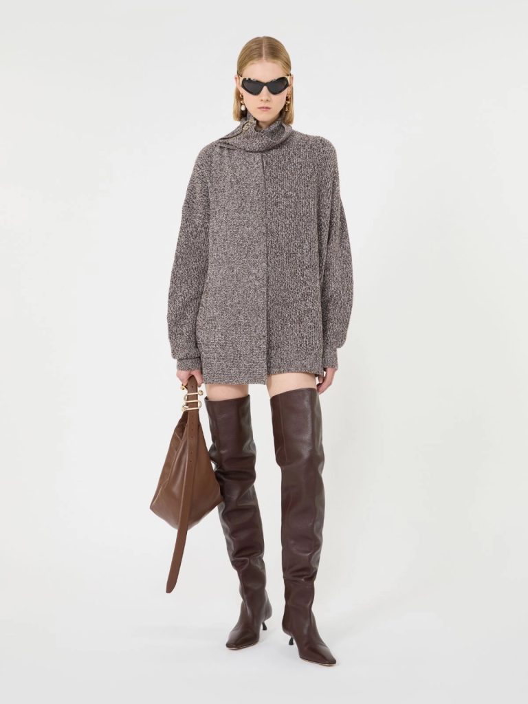 Model wearing an oversized gray knit turtleneck sweater dress with knee-high brown leather boots and a brown handbag, accessorized with sunglasses.