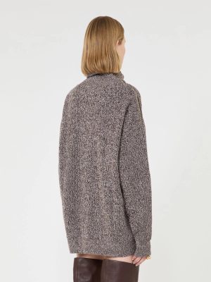 Back view of a person wearing a long grey tweed coat with a shoulder zip, paired with dark brown knee-high boots.