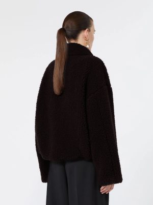 Back view of a person wearing a black teddy coat, hair in a ponytail, with gold earrings, against a light background.