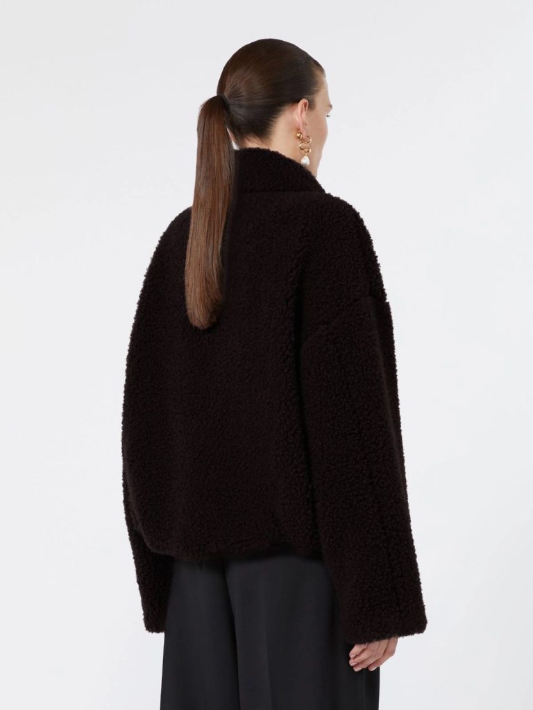 Back view of a person wearing a black teddy coat, hair in a ponytail, with gold earrings, against a light background.