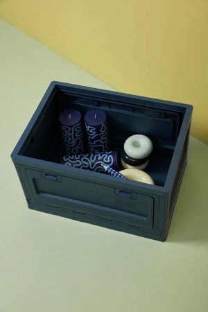 Open dark blue storage box containing two tall patterned blue candles and white ceramic bowls on a pale yellow-green surface.