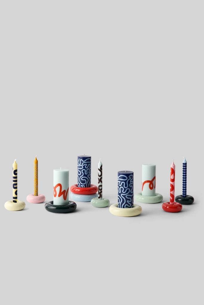 Row of colorful decorative candles with patterned bodies on round bases, against a gray backdrop.