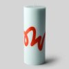 Image 563 - New Trend Tall pale blue pillar candle with a red cursive design wrapping around the side, unlit and standing on a soft shadowed surface.