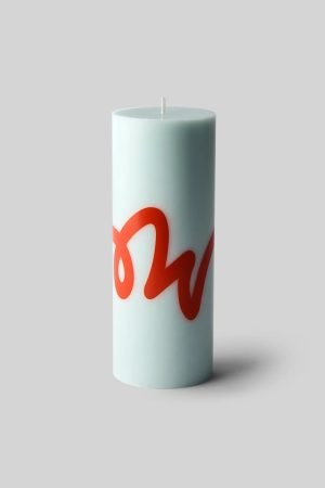 Tall pale blue pillar candle with a red cursive design wrapping around the side, unlit and standing on a soft shadowed surface.