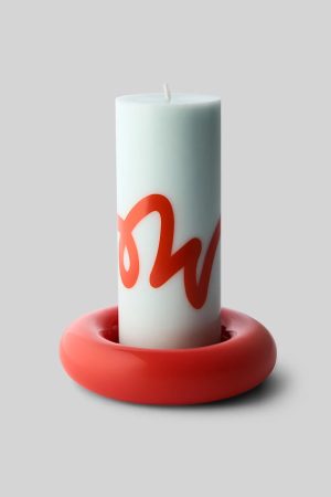 White pillar candle with a red cursive design resting in a glossy red donut-shaped holder on a gray background.