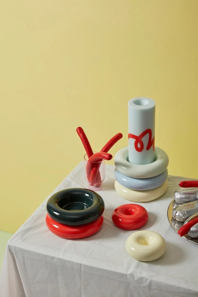 Stack of glossy pastel ceramic rings with red curved pieces and a pale yellow backdrop on a white tablecloth.